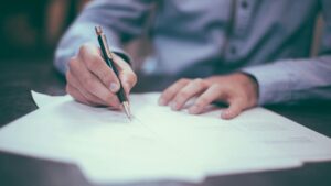Nahaufnahme einer Person, die mit einem Stift Notizen auf mehreren ausgebreiteten Dokumenten festhält.